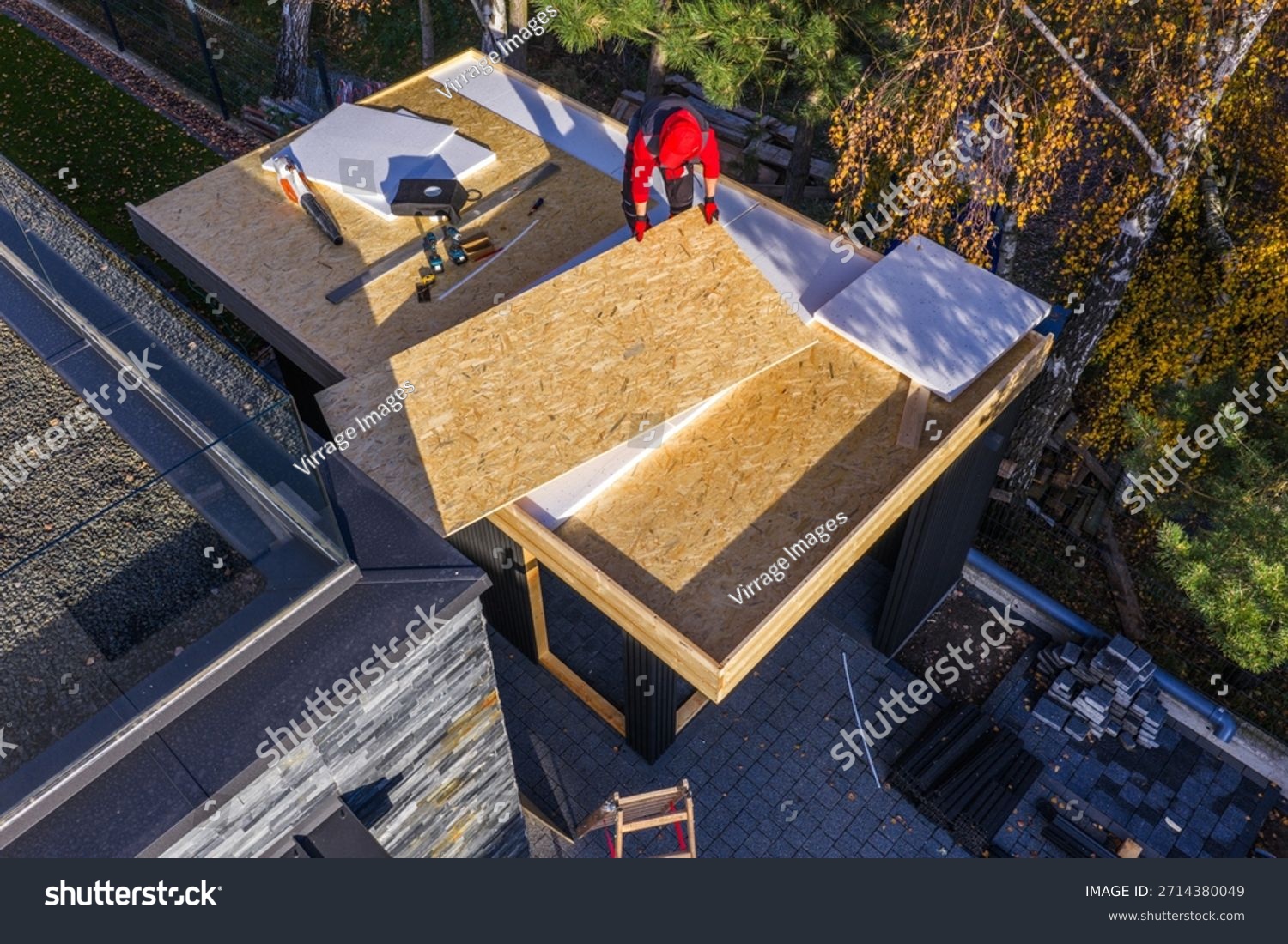 stock-photo-a-worker-places-roof-panels-on-a-home-under-construction-the-setting-is-a-neighborhood-with-trees-2714380049
